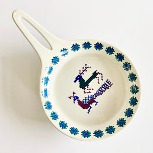 Pu&ograve; includere: Un piatto da portata in ceramica bianca con un bordo floreale blu e verde. Il piatto presenta un design stilizzato di un cervo e un uccello al centro.