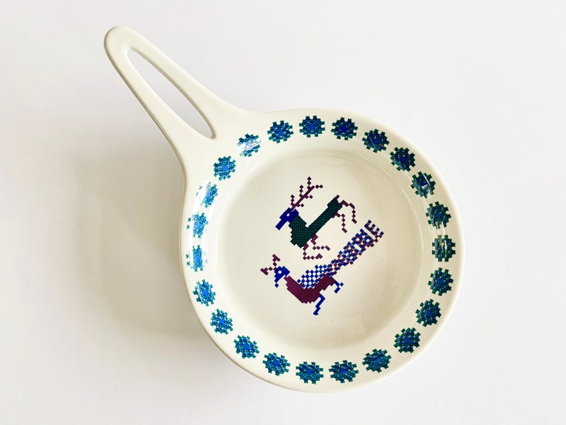 Pu&ograve; includere: Un piatto da portata in ceramica bianca con un bordo floreale blu e verde. Il piatto presenta un design stilizzato di un cervo e un uccello al centro.