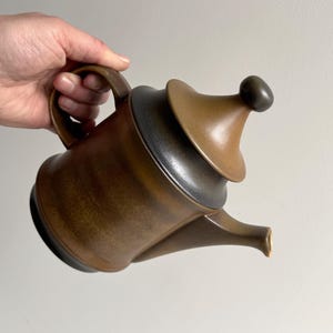May include: A brown ceramic teapot with a lid and a spout. The teapot has a dark brown glaze and a light brown glaze.