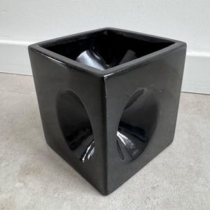 Pode incluir: Um vaso quadrado de cerâmica preta brilhante com recortes arredondados em dois lados. O vaso tem um design moderno e uma superfície lisa e reflexiva. Adequado para uso interno ou externo.