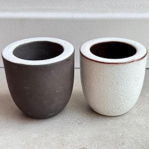 May include: Two ceramic cups, one black with a white rim and one white with a brown rim.