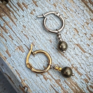May include: A pair of hoop earrings with a dangling pyrite stone. The earrings are made of silver and gold metal. The pyrite stones are a dark gray color.