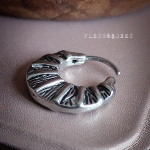 May include: Silver hoop earring with a textured, geometric design. The earring is made of stainless steel and has a hinged closure.