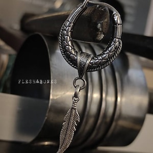 Puede incluir: Un aro de plata para la oreja con un dise&ntilde;o texturizado y un colgante de pluma. El aro est&aacute; hecho de metal y tiene un acabado oxidado oscuro.