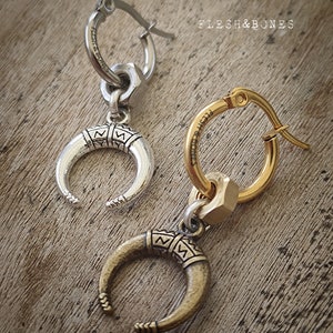 May include: Two silver and gold hoop earrings with a crescent moon charm. The charms have a detailed design and are attached to the hoops with a small ring. The hoops are marked with the text "Flesh & Bones".