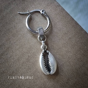 Può includere: Orecchino a cerchio in argento con ciondolo a conchiglia di cauri in argento. L'orecchino è contrassegnato con "Flesh & Bones".