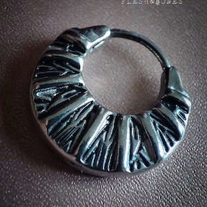May include: Silver hoop earring with a textured, geometric design. The earring is a simple circle with a raised pattern.