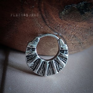 May include: Silver hoop earring with a textured, geometric design. The earring is circular and has a slightly curved shape.