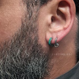 Könnte beinhalten: Nahaufnahme eines Ohrs mit zwei Ohrringen. Einer ist ein kleiner Silberreif mit türkisfarbener Einlage. Der andere ist ein kleiner Silberreif mit strukturiertem Design. Der Text "FLESH&BONES" ist sichtbar.