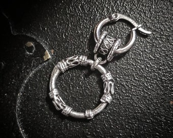 Puede incluir: Un pendiente de aro de plata con un colgante circular decorativo. El colgante tiene un diseño texturizado y está unido al aro con un pequeño anillo de plata.