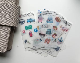 May include: A set of translucent planner stickers featuring travel-themed illustrations. The sheets include icons for Roads & Rides, Voyage Prep, and Tables Abroad, with small circles for tracking and lines for recording dollar amounts for each item.