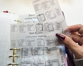 May include: Clear, transparent sticky note challenge sheets with handwritten text, designed to track savings. The sheets are held in a binder, with the text "Save $5,000 Sticky note challenge". Each month has a savings goal.