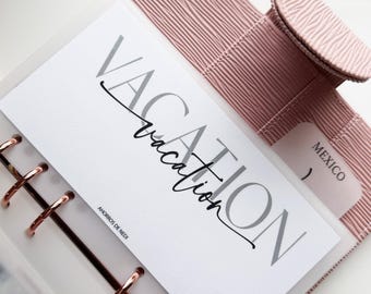 May include: A light pink planner with a textured cover and rose gold rings. A white insert displays the word "VACATION" in gray and black script. A small tab reads "MEXICO". The planner is open, revealing the insert.
