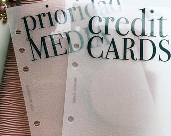 May include: Two translucent, frosted plastic planner dividers with six punched holes along the left edge. The top divider features the black text "priority" and "MEDIA" while the bottom divider displays "credit" and "CARDS" in a bold serif font.