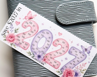 May include: A white rectangular savings challenge card with the text Save $2027 in 2027 and AHORROS DE NEDI. The card features large pink and purple numbers filled with dollar amounts, decorated with watercolor butterflies, hearts, and floral accents.