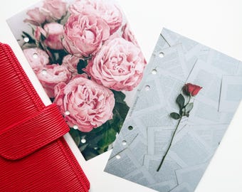 May include: A red leather planner next to two decorative planner inserts. One insert features a bouquet of pink roses, and the other has a single red rose on a background of printed text. Both inserts have pre-punched holes.