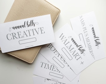 May include: White cards with the words "annual bills" and various company names in gray, including "CREATIVE" and "WALMART +." A beige, textured wallet is in the background.