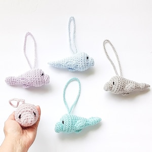 May include: A collection of handmade crochet seal ornaments in various pastel colors: pink, light blue, lavender, and gray. Each seal has a loop for hanging and small black bead eyes. The seals are displayed on a white background.