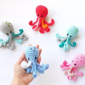 May include: Five crocheted octopus plushies in different colors: gray, red, blue, turquoise, and pink. Each octopus has eight tentacles and a small, embroidered face.