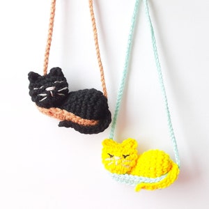 May include: Two crocheted cat necklaces, one black and one yellow, hanging from brown and blue cords.
