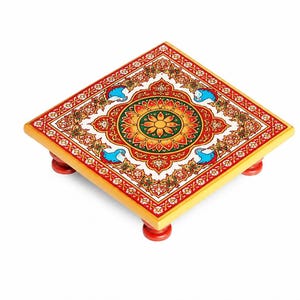 May include: A square wooden platform with four short red legs, featuring a vibrant top surface decorated with a central floral mandala pattern in yellow, orange, and green, surrounded by intricate red, white, and blue peacock motifs.