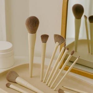 May include: A collection of makeup brushes with cream-colored handles and brown bristles. The brushes are arranged on a matching tray, with a mirror in the background reflecting some of the brushes. The set includes various brush sizes and shapes.