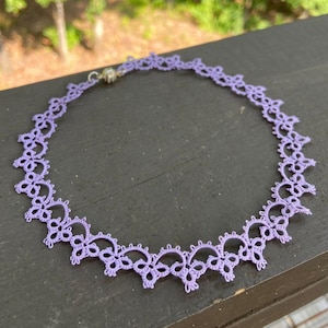 May include: A delicate lavender lace choker necklace with a silver clasp. The necklace is made of fine, intricate lace and has a delicate, feminine look.