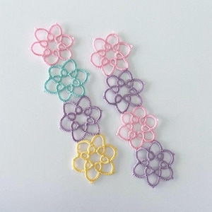 以下が含まれることがあります： ピンク、パープル、イエロー、ブルーなど、パステルカラーの繊細なクロシェレースの花が6つセットになっています。花は縦に並べられており、一番上の花が大きく、一番下の花が小さいです。