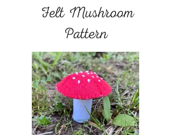 May include: A red felt mushroom with white spots on top of a white felt stem. The mushroom is sitting on a bed of green grass.