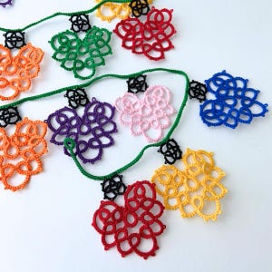 May include: A colorful garland of crocheted hearts in various colors, including orange, green, red, purple, pink, blue, and yellow. The hearts are connected by a green string.