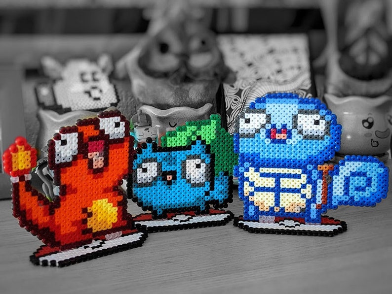 Puede incluir: Tres figuras de pixel art hechas de cuentas de colores. Las figuras son un Pok&eacute;mon de tipo fuego rojo y naranja, un Pok&eacute;mon de tipo agua azul y verde, y un Pok&eacute;mon azul y blanco parecido a una tortuga.