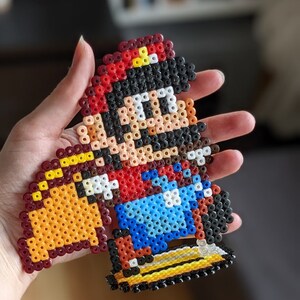May include: A pixel art bead sprite of Super Mario, wearing a red hat and overalls, riding a yellow Yoshi. The bead sprite is made with colorful plastic beads.