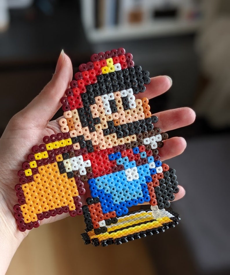 May include: A pixel art bead sprite of Super Mario, wearing a red hat and overalls, riding a yellow Yoshi. The bead sprite is made with colorful plastic beads.