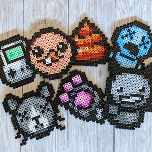 May include: A set of 8 pixel art keychains featuring various characters and designs. The keychains are made of colorful plastic beads and include a grey Game Boy, a pink and white character, a grey and white dog, a purple and pink character, a grey and white character, a blue and white character, a brown and orange character, and a red and orange character.