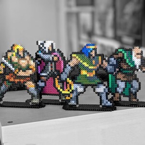 May include: Four pixel art figures made of colourful beads, depicting characters from a video game. The figures are standing on black bases and are arranged in a row. The figures are a warrior with a sword, a wizard with a staff, a knight with a shield, and a mage with a spellbook.