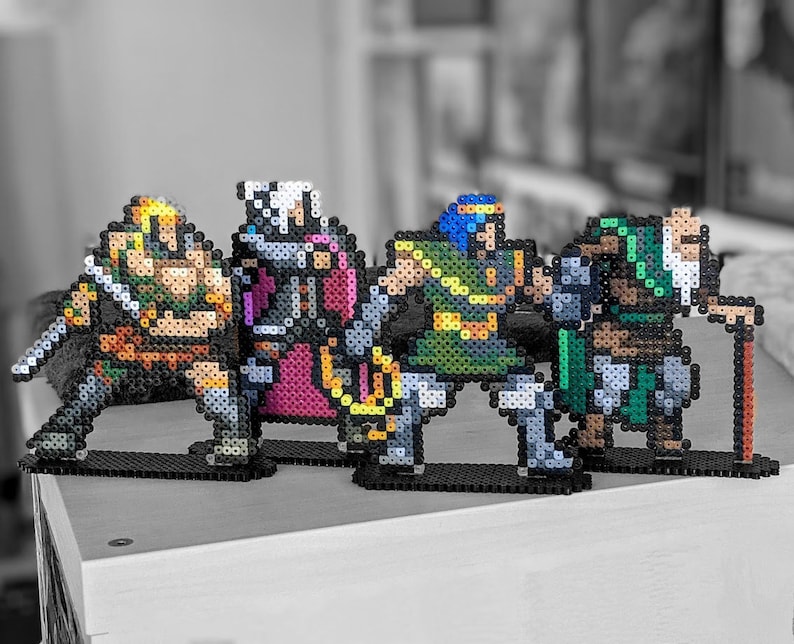 May include: Four pixel art figures made of colourful beads, depicting characters from a video game. The figures are standing on black bases and are arranged in a row. The figures are a warrior with a sword, a wizard with a staff, a knight with a shield, and a mage with a spellbook.