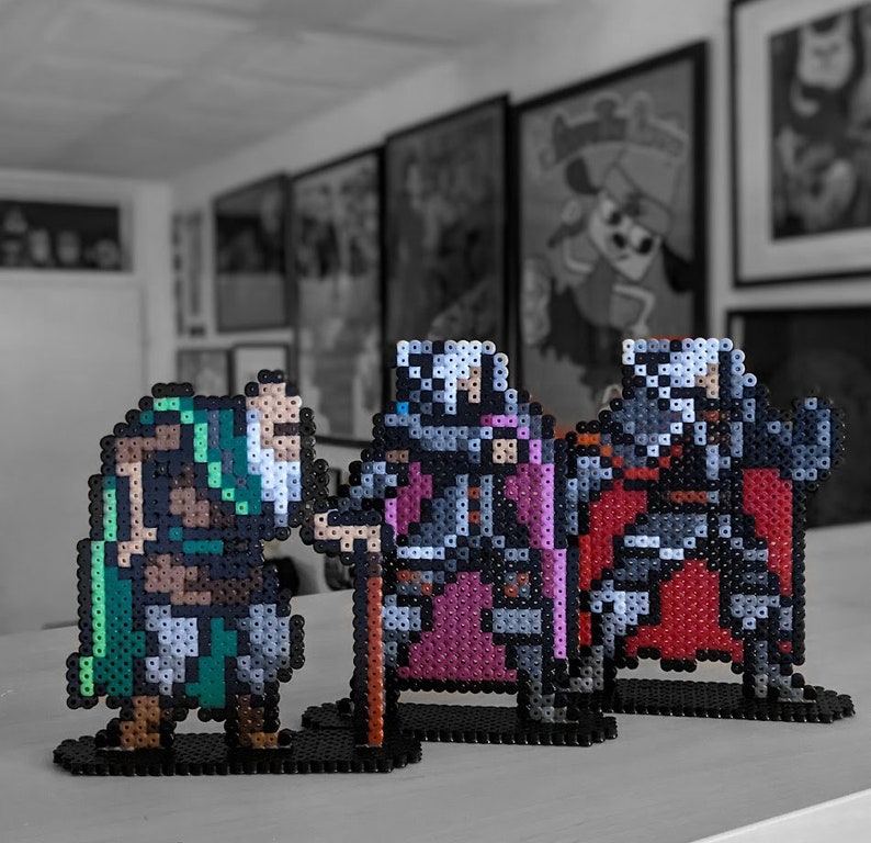 May include: Three pixel art figures made of beads. The figures are a green and brown warrior, a purple and gray knight, and a red and gray knight. The figures are standing on black bases.