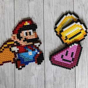 May include: A pixel art character of Mario from the Super Mario Bros. video game series. Mario is wearing a red hat, blue overalls, and white gloves. He is holding a yellow brick block. The image also includes a pixel art image of a golden coin and a pink star.
