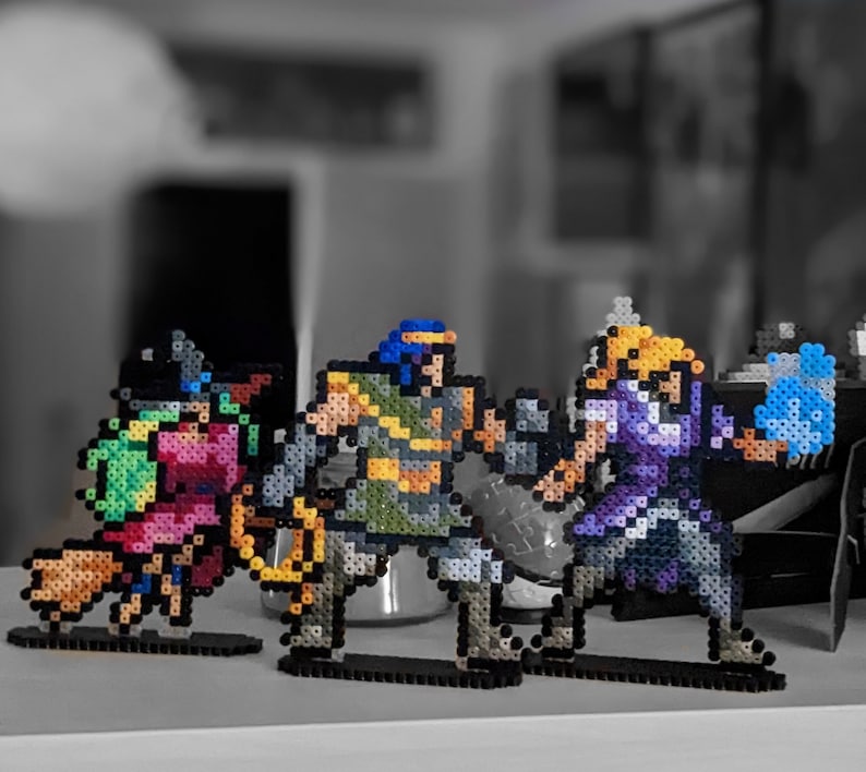 May include: Four pixel art figures made of colourful beads. The figures are standing on black bases. The figures are a blue and green wizard, a purple and blue warrior, a green and yellow warrior, and a red and green warrior.