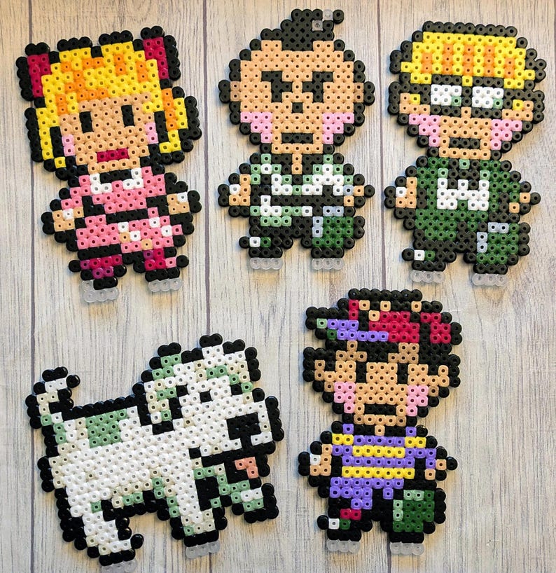 Pu&ograve; includere: Cinque personaggi in pixel art e un cane realizzati con perline Perler colorate. I personaggi includono una ragazza con i capelli biondi e un vestito rosa, un ragazzo con i capelli castani e una camicia verde, un ragazzo con i capelli biondi e una camicia verde, un ragazzo con i capelli castani e una camicia viola, e un cane bianco.