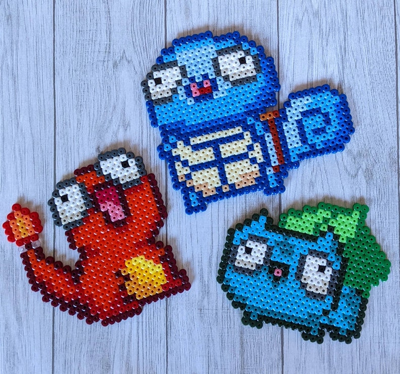 Puede incluir: Tres personajes de pixel art hechos con cuentas de colores. El primer personaje es azul con un cuerpo blanco y amarillo y una cabeza grande y redonda con dos ojos negros. El segundo personaje es rojo con un cuerpo amarillo y naranja y una cabeza grande y redonda con dos ojos negros. El tercer personaje es azul con una cabeza verde y un cuerpo blanco con dos ojos negros.