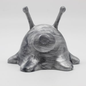 May include: A silver-colored, 3D printed figurine of a slug with two long antennae. The slug has a textured, marbled surface.