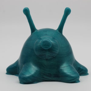 May include: A teal blue, 3D printed, slug-like creature with two long, thin antennae. The creature has a smooth, glossy finish.