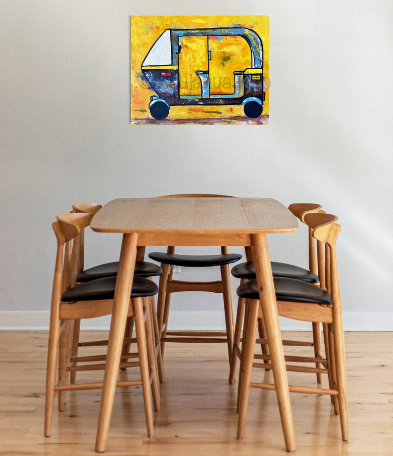 May include: An abstract painting of a yellow and black auto-rickshaw on a yellow background. The artwork is displayed above a wooden dining table with six chairs. The chairs have black seats and light wood frames.