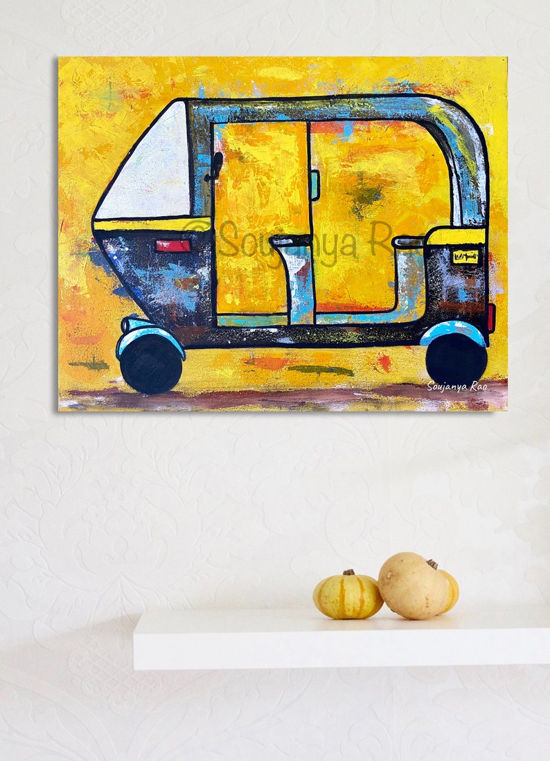 May include: An abstract painting of an auto-rickshaw, or tuk-tuk, in shades of yellow, blue, and black. The artwork features the text "Soujanya Rao" in the lower right corner. Two small pumpkins sit on a white shelf below the painting.