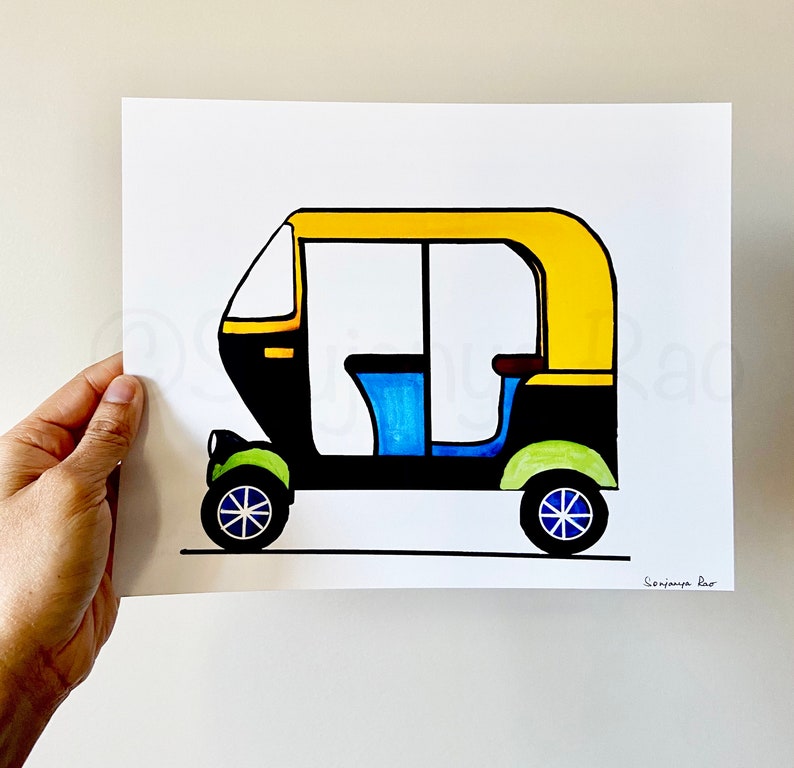 May include: A colorful illustration of an auto rickshaw, featuring a yellow roof, black body, and blue and green accents. The artwork is on white paper and held by a hand.