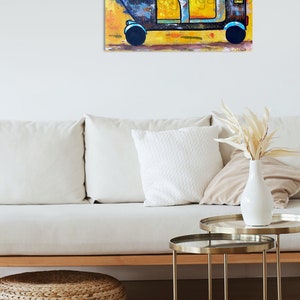 May include: A colorful painting of an auto rickshaw, or tuk-tuk, against a yellow background. The vehicle is primarily blue and yellow, with black wheels. The artwork is displayed on a wall above a white sofa and decorative tables.