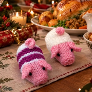 May include: Two small, hand-knitted pig figurines. One pig is white with a purple striped body and a pink snout, ears, and tail. The other pig is entirely white with a pink snout, ears, tail, and a small pink tuft on its back. Both have black eyes.