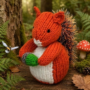May include: A knitted squirrel toy with bright orange yarn, a white belly, and a textured black and orange tail. The squirrel holds a small green and grey knitted acorn in its paws. The toy features two small black eyes and pointed ears.