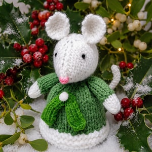Op de afbeelding: Een gehaakt muisfiguurtje met witte vacht, een roze neus en zwarte ogen. De muis draagt een groene gebreide trui met een wit pompondetail bij de halslijn en een witte gebreide zoom, voorzien van witte mouwen en een witte staart.